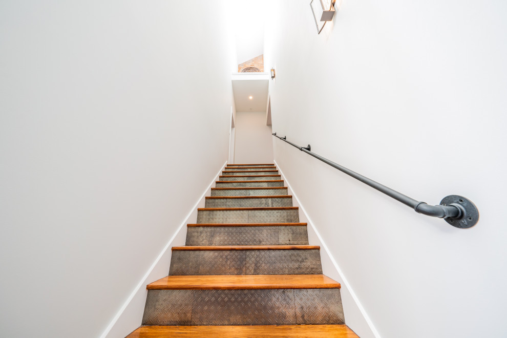 Cette image montre un grand escalier droit minimaliste avec des marches en bois, des contremarches carrelées et un garde-corps en métal.