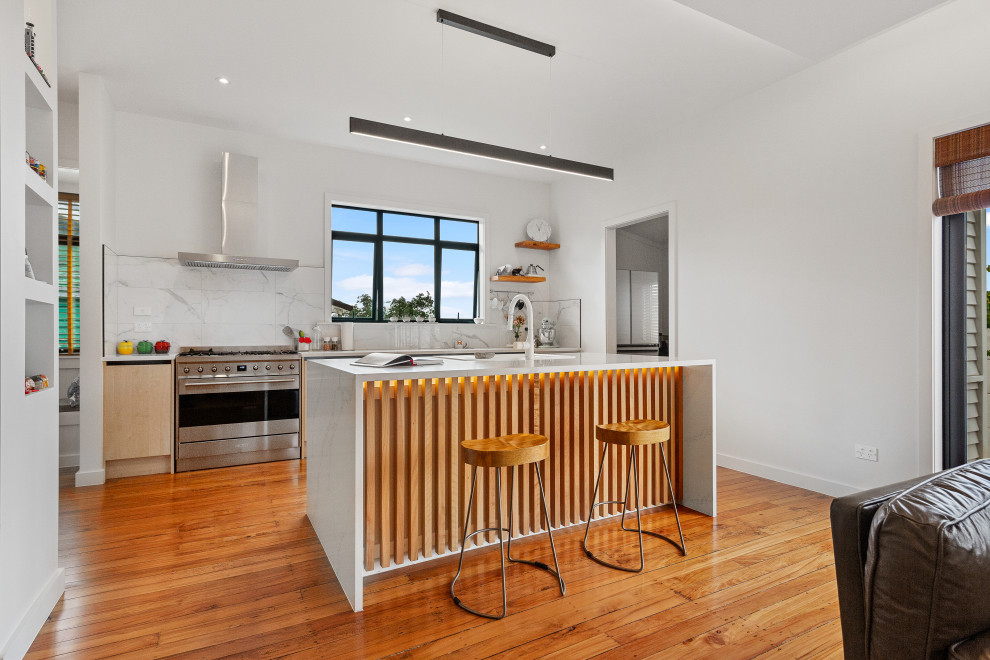 Photo of a contemporary kitchen in Auckland with an undermount sink, quartz benchtops, white splashback, stainless steel appliances, medium hardwood floors, with island, brown floor and white benchtop.