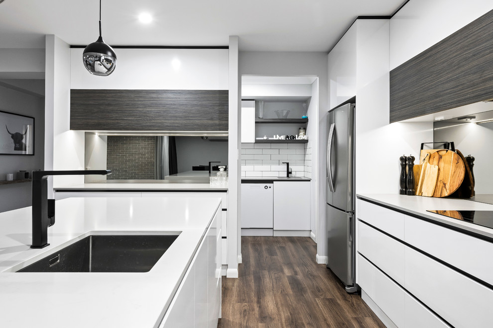 Inspiration for a mid-sized contemporary galley open plan kitchen in Other with an undermount sink, flat-panel cabinets, white cabinets, quartz benchtops, metallic splashback, mirror splashback, stainless steel appliances, laminate floors, with island, brown floor and white benchtop.