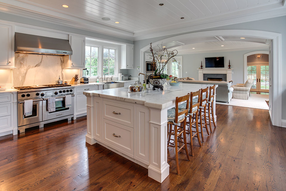 Photo of an expansive traditional u-shaped open plan kitchen in Other with a farmhouse sink, recessed-panel cabinets, white cabinets, stainless steel appliances, with island, brown floor, marble benchtops, white splashback, marble splashback and medium hardwood floors.