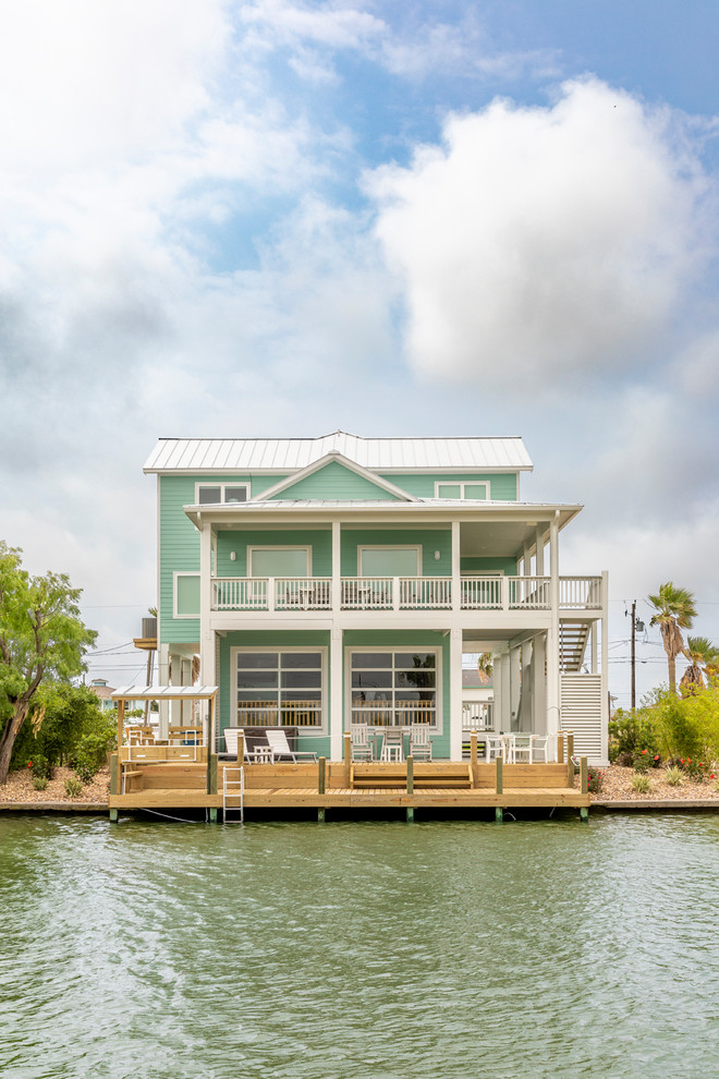 Inspiration for a large beach style two-storey blue house exterior in Houston with vinyl siding, a hip roof and a metal roof.