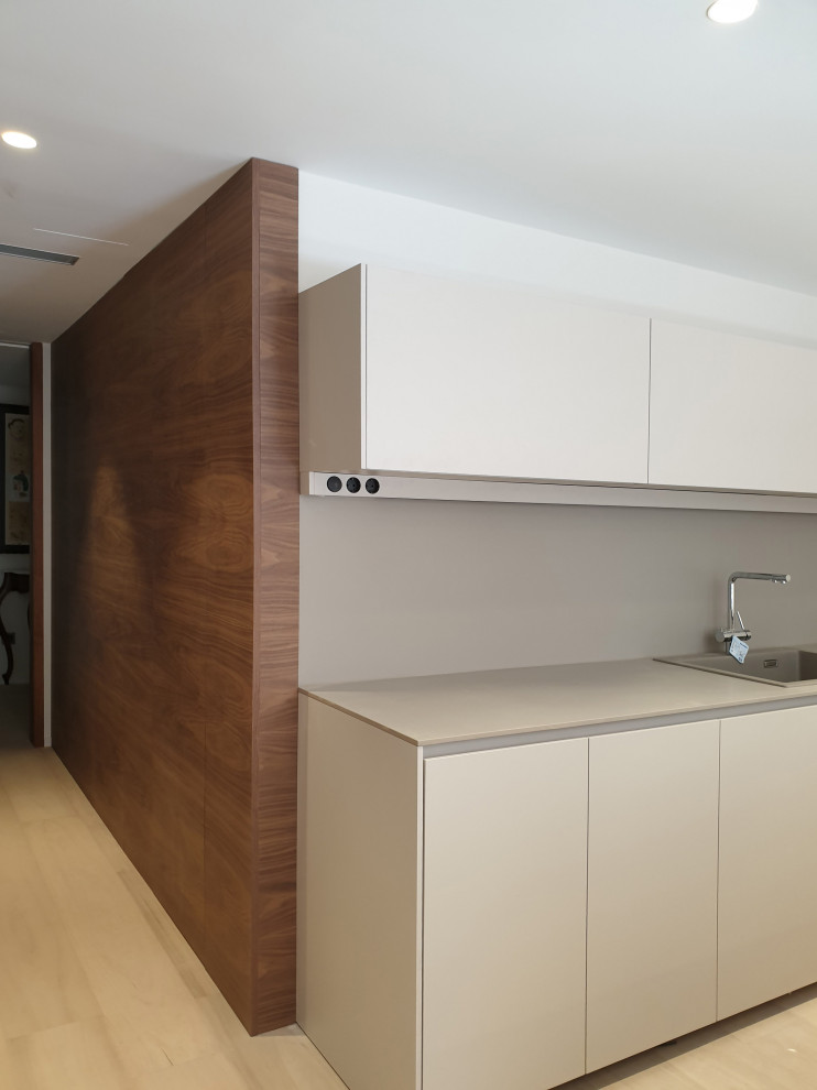Design ideas for a large single-wall eat-in kitchen in Valencia with a single-bowl sink, flat-panel cabinets, medium wood cabinets, limestone benchtops, grey splashback, limestone splashback, black appliances, laminate floors, a peninsula, brown floor and grey benchtop.