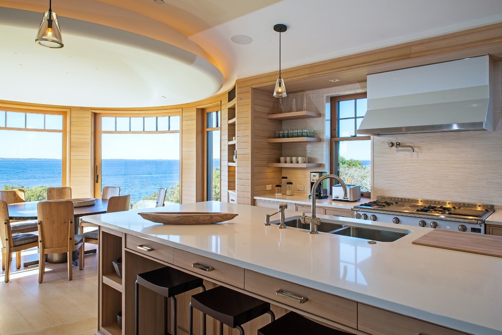 Design ideas for a beach style galley eat-in kitchen in Boston with an undermount sink, flat-panel cabinets, light wood cabinets, light hardwood floors, with island, beige splashback, stainless steel appliances and white benchtop.