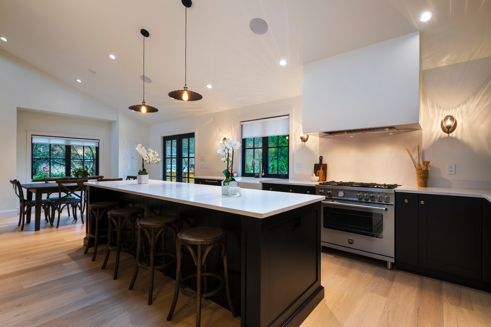Mid-sized mountain style l-shaped light wood floor and beige floor open concept kitchen photo in Vancouver with a farmhouse sink, shaker cabinets, black cabinets, quartz countertops, paneled appliances, an island and white countertops
