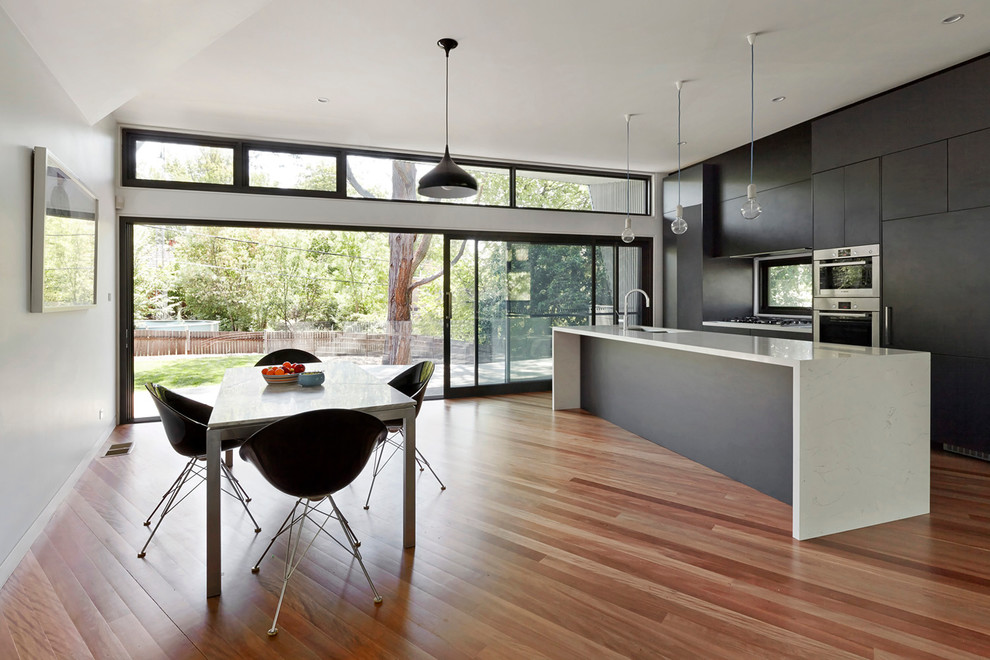 This is an example of a contemporary galley eat-in kitchen in Melbourne with flat-panel cabinets, black cabinets, stainless steel appliances, medium hardwood floors and with island.
