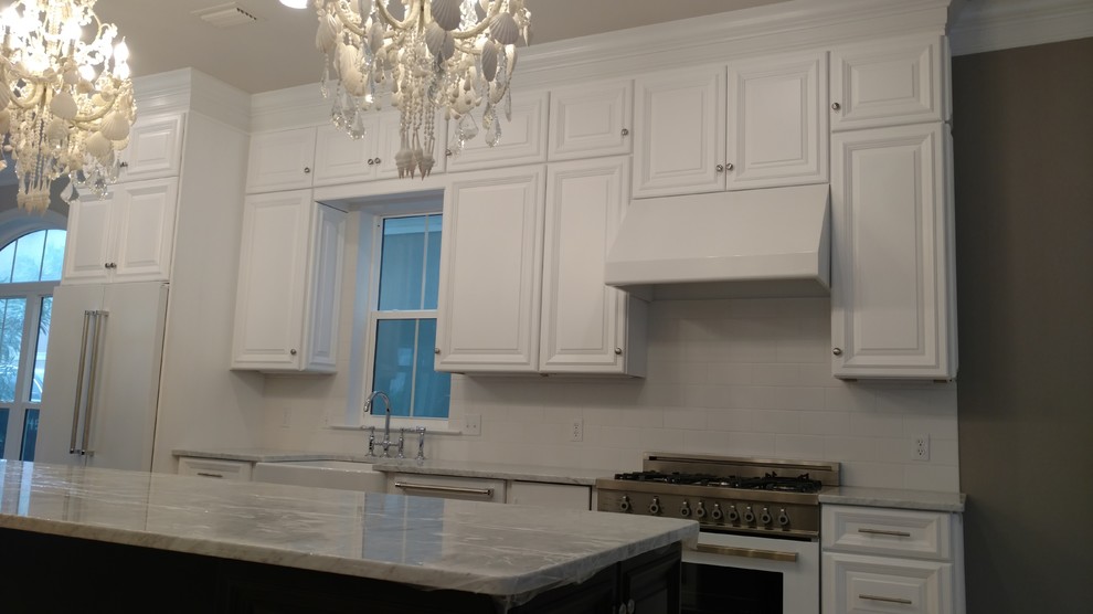 Medium sized coastal single-wall kitchen/diner in Miami with a belfast sink, raised-panel cabinets, white cabinets, marble worktops, white splashback, ceramic splashback, white appliances, travertine flooring and an island.