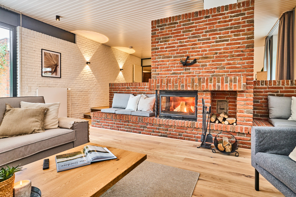Идея дизайна: гостиная комната в скандинавском стиле с бежевыми стенами, печью-буржуйкой, фасадом камина из кирпича, телевизором на стене, коричневым полом, потолком из вагонки и обоями на стенах