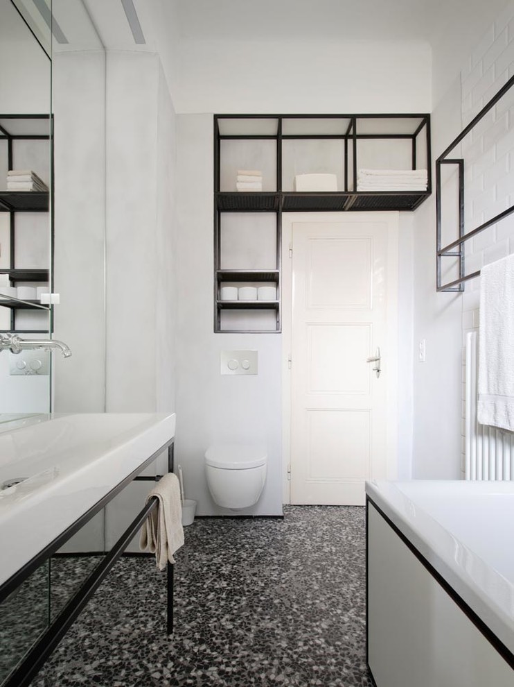Photo of a mid-sized contemporary bathroom in Munich with a freestanding tub, a wall-mount toilet, white tile, ceramic tile, white walls, concrete floors and a trough sink.