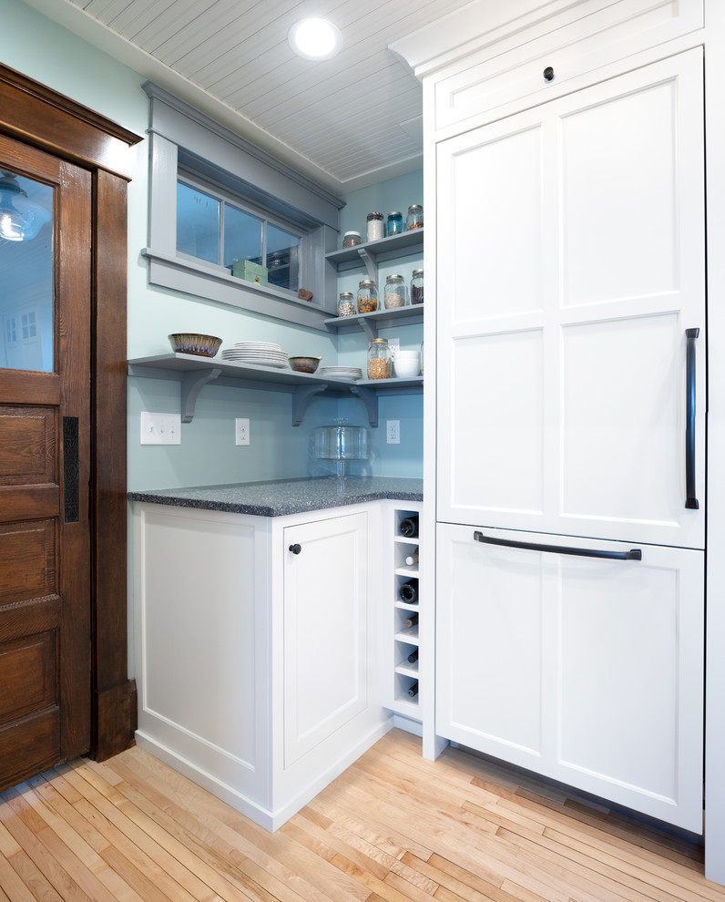 Inspiration for a mid-sized traditional u-shaped eat-in kitchen in Minneapolis with a farmhouse sink, shaker cabinets, white cabinets, recycled glass benchtops, white splashback, subway tile splashback, panelled appliances, light hardwood floors, a peninsula, brown floor and grey benchtop.