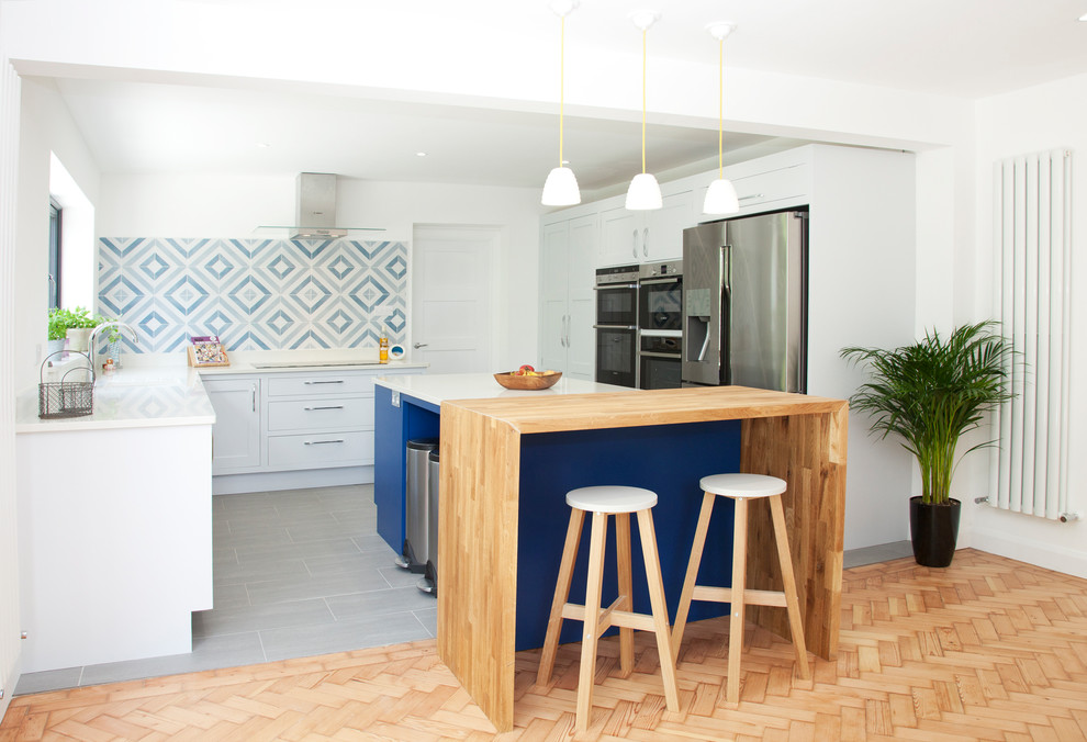 Photo of a mid-sized contemporary kitchen in London with flat-panel cabinets, white cabinets, multi-coloured splashback, stainless steel appliances, with island, grey floor and white benchtop.