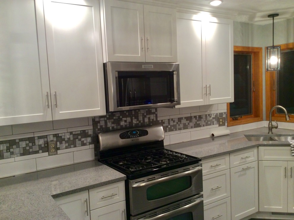 Photo of a mid-sized transitional l-shaped separate kitchen in Chicago with an undermount sink, shaker cabinets, white cabinets, solid surface benchtops, white splashback, ceramic splashback, stainless steel appliances, ceramic floors, with island and grey floor.