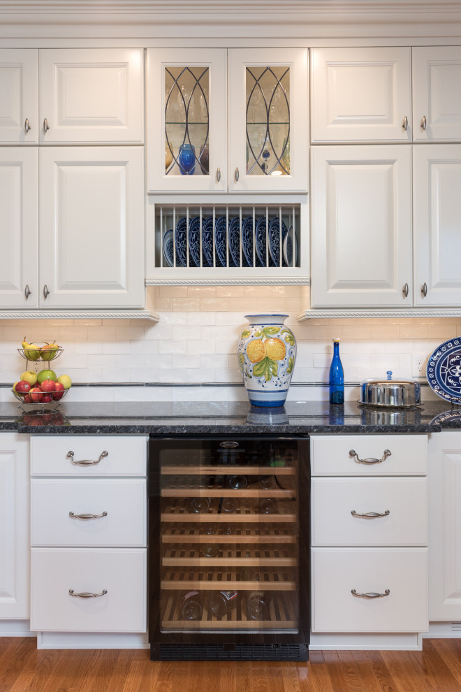 Large transitional single-wall light wood floor and brown floor open concept kitchen photo with a farmhouse sink, raised-panel cabinets, white cabinets, quartz countertops, white backsplash, ceramic backsplash, stainless steel appliances, an island and white countertops