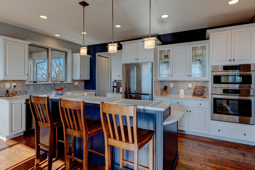 Inspiration for a large contemporary u-shaped eat-in kitchen in Charlotte with a drop-in sink, beaded inset cabinets, white cabinets, granite benchtops, blue splashback, mosaic tile splashback, stainless steel appliances, medium hardwood floors, with island, brown floor, white benchtop and wood.