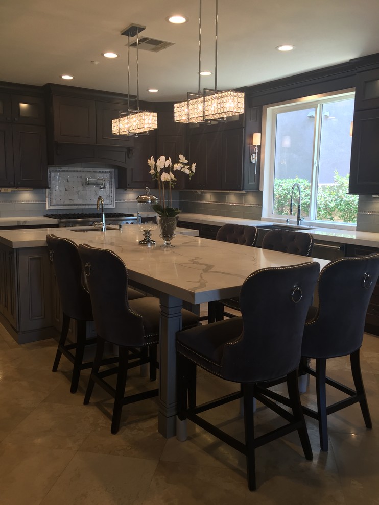 Inspiration for a mid-sized transitional l-shaped travertine floor and beige floor enclosed kitchen remodel in Orange County with a farmhouse sink, brown cabinets, marble countertops, gray backsplash, glass tile backsplash, stainless steel appliances and an island