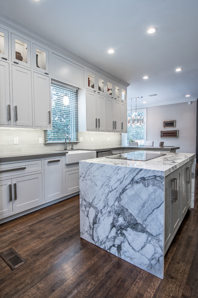 Large transitional l-shaped dark wood floor enclosed kitchen photo with a farmhouse sink, shaker cabinets, white cabinets, solid surface countertops, white backsplash, subway tile backsplash, stainless steel appliances and an island