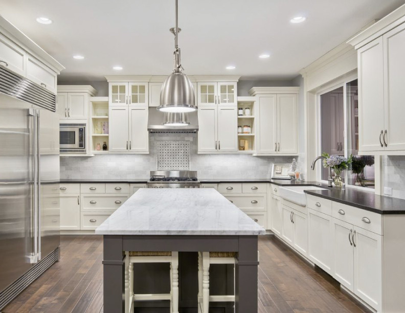 This is an example of a mid-sized contemporary kitchen in Los Angeles with a farmhouse sink, shaker cabinets, white cabinets, marble benchtops, grey splashback, marble splashback, stainless steel appliances, porcelain floors, with island, brown floor and black benchtop.