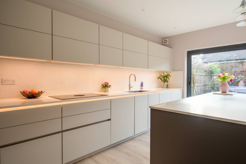 This is an example of a large contemporary l-shaped open plan kitchen in Hertfordshire with a double-bowl sink, flat-panel cabinets, white cabinets, quartzite benchtops, black appliances, with island, white benchtop and exposed beam.