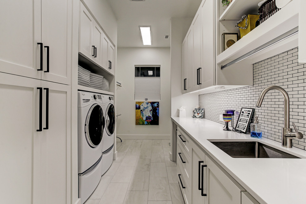 Photo of a transitional galley laundry room in Houston with an undermount sink, shaker cabinets, white cabinets, white walls, a side-by-side washer and dryer, grey floor and white benchtop.