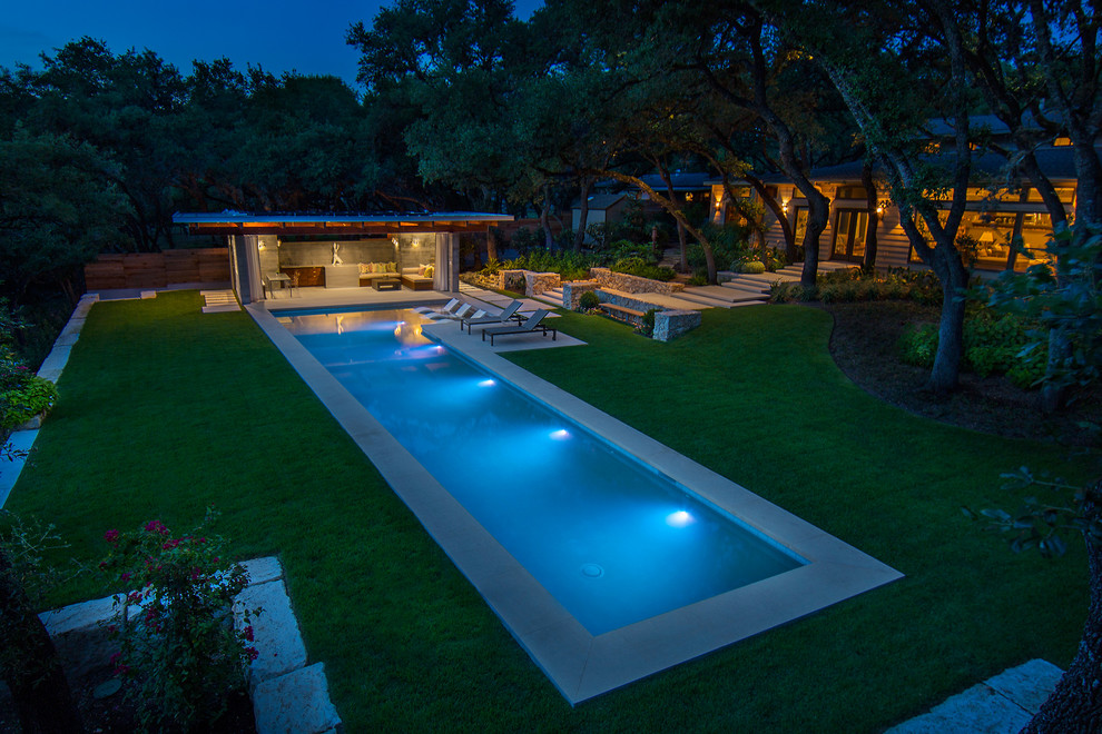 Large modern backyard rectangular lap pool in Austin with a pool house and natural stone pavers.