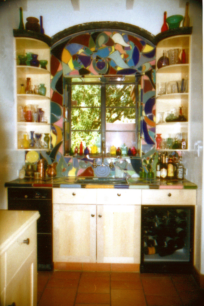 Inspiration for a mid-sized eclectic l-shaped kitchen pantry in Phoenix with shaker cabinets, light wood cabinets, tile benchtops, multi-coloured splashback, ceramic splashback, black appliances and terra-cotta floors.