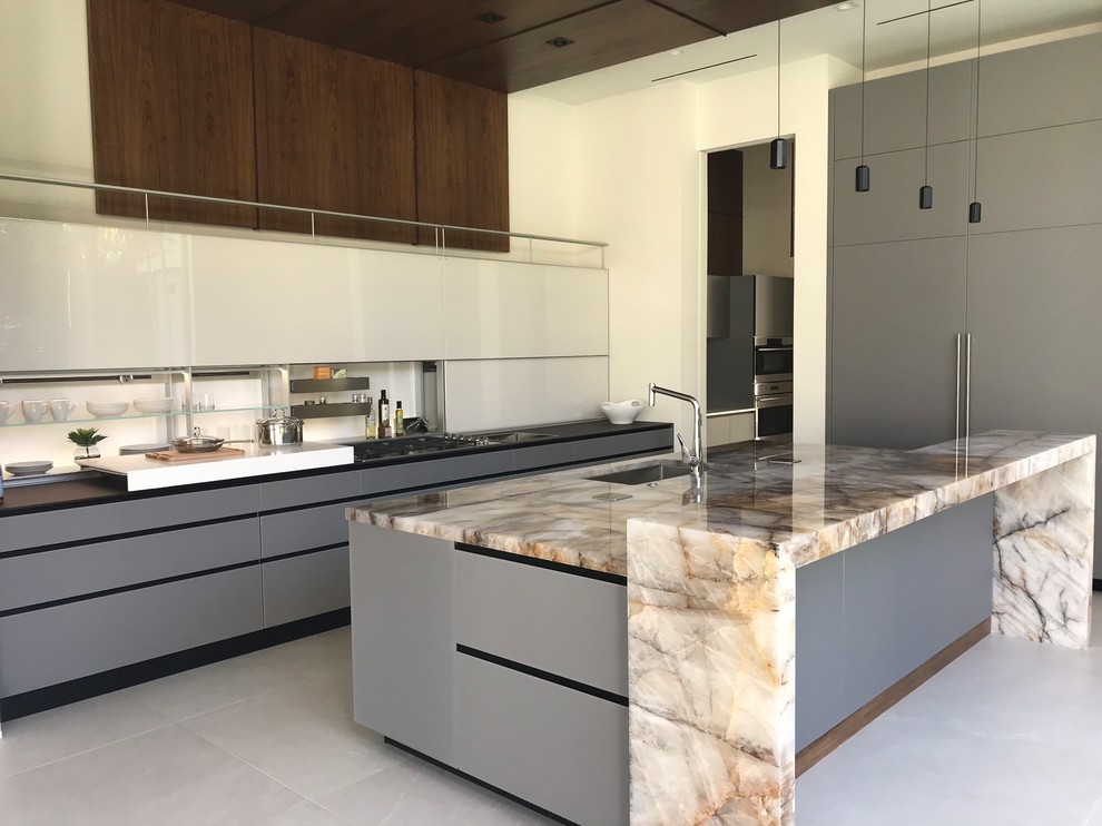 Large contemporary single-wall open plan kitchen in Miami with an undermount sink, flat-panel cabinets, grey cabinets, onyx benchtops, white splashback, panelled appliances, concrete floors, with island and grey floor.