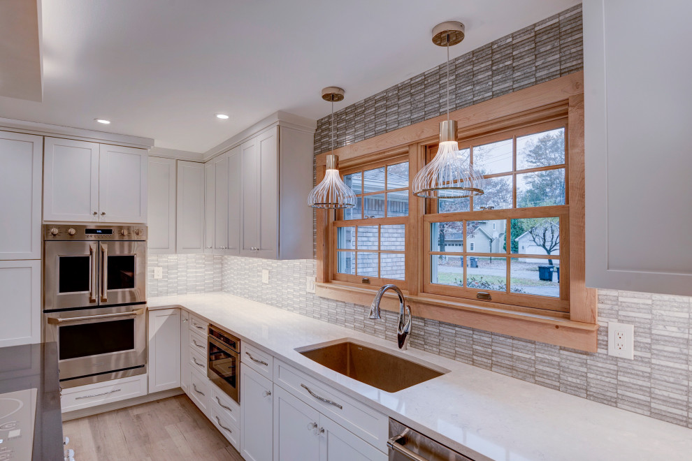 Example of a large transitional u-shaped light wood floor and beige floor open concept kitchen design in New York with an undermount sink, shaker cabinets, white cabinets, quartzite countertops, white backsplash, ceramic backsplash, stainless steel appliances, an island and white countertops