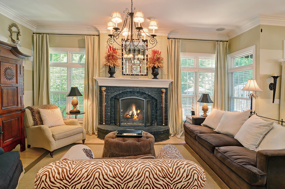 This is an example of a traditional open concept family room in Chicago with beige walls, a standard fireplace, a brick fireplace surround, light hardwood floors and a concealed tv.