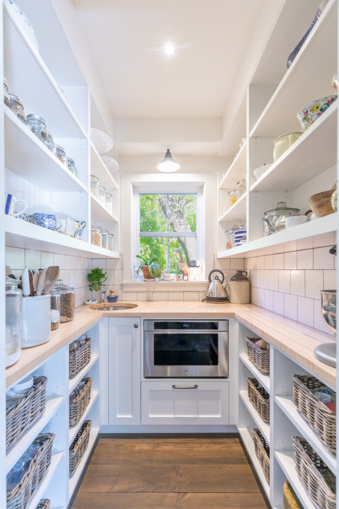 Photo of a transitional u-shaped kitchen pantry in Other with an undermount sink, shaker cabinets, white cabinets, wood benchtops, white splashback, subway tile splashback, stainless steel appliances, medium hardwood floors, no island, brown floor and beige benchtop.