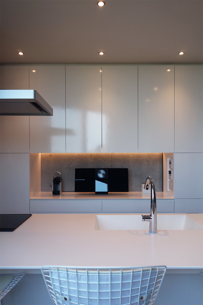 Photo of a modern single-wall open plan kitchen in Tokyo with an integrated sink, beaded inset cabinets, white cabinets, solid surface benchtops, black appliances, light hardwood floors, with island, white floor and white benchtop.