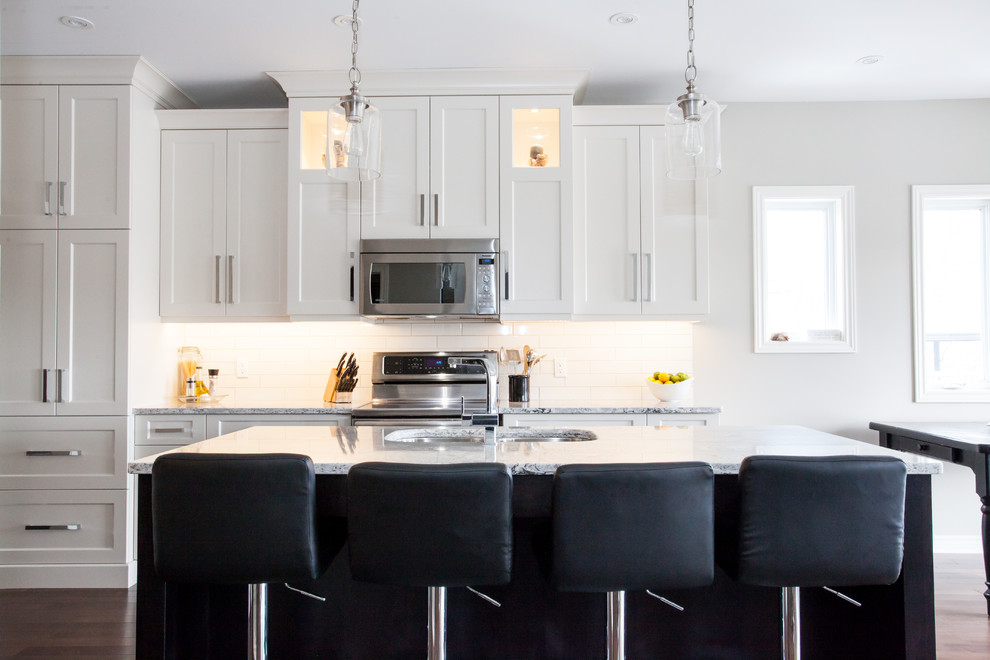 Large transitional u-shaped dark wood floor and brown floor eat-in kitchen photo in Toronto with an undermount sink, shaker cabinets, white cabinets, quartz countertops, white backsplash, subway tile backsplash, stainless steel appliances, an island and white countertops
