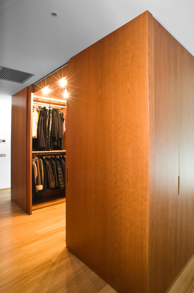 Mid-sized contemporary gender-neutral walk-in wardrobe in Milan with open cabinets, medium wood cabinets and light hardwood floors.