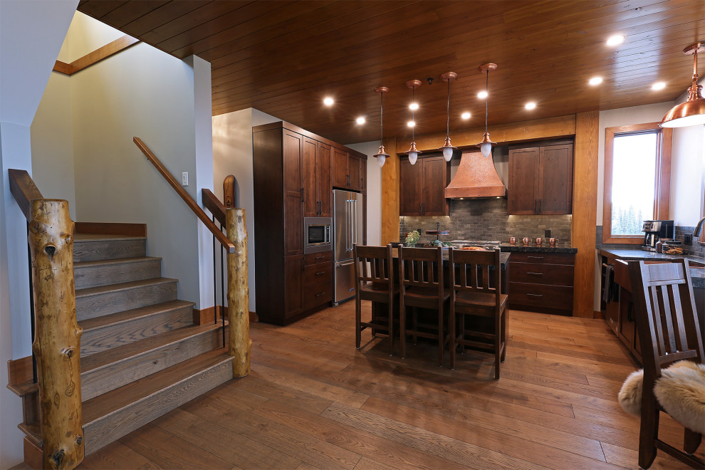 Inspiration for a rustic medium tone wood floor, brown floor and wood ceiling open concept kitchen remodel with a farmhouse sink, shaker cabinets, medium tone wood cabinets, quartzite countertops, black backsplash, slate backsplash, stainless steel appliances, an island and black countertops