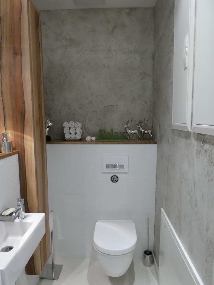 Gästetoilette mit Wandtoilette mit Spülkasten, weißen Fliesen, Mosaikfliesen, grauer Wandfarbe, Wandwaschbecken und weißem Boden in Munich