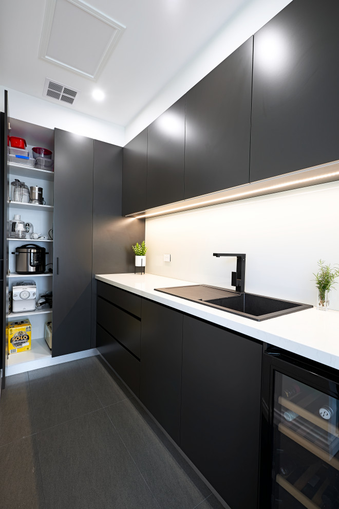 This is an example of a modern u-shaped separate kitchen in Melbourne with a drop-in sink, flat-panel cabinets, black cabinets, quartz benchtops, white splashback, glass sheet splashback, black appliances, porcelain floors, with island, grey floor and white benchtop.