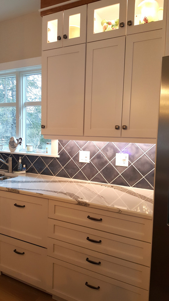Photo of a large classic l-shaped kitchen/diner in Portland Maine with a submerged sink, recessed-panel cabinets, white cabinets, engineered stone countertops, blue splashback, porcelain splashback, stainless steel appliances, light hardwood flooring, an island and white worktops.