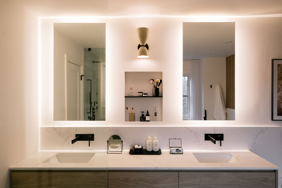 This is an example of a large modern ensuite bathroom in Toronto with flat-panel cabinets, light wood cabinets, a freestanding bath, a built-in shower, a wall mounted toilet, white tiles, stone slabs, white walls, porcelain flooring, a submerged sink, quartz worktops, grey floors, a hinged door, white worktops, a wall niche, double sinks, a floating vanity unit and panelled walls.