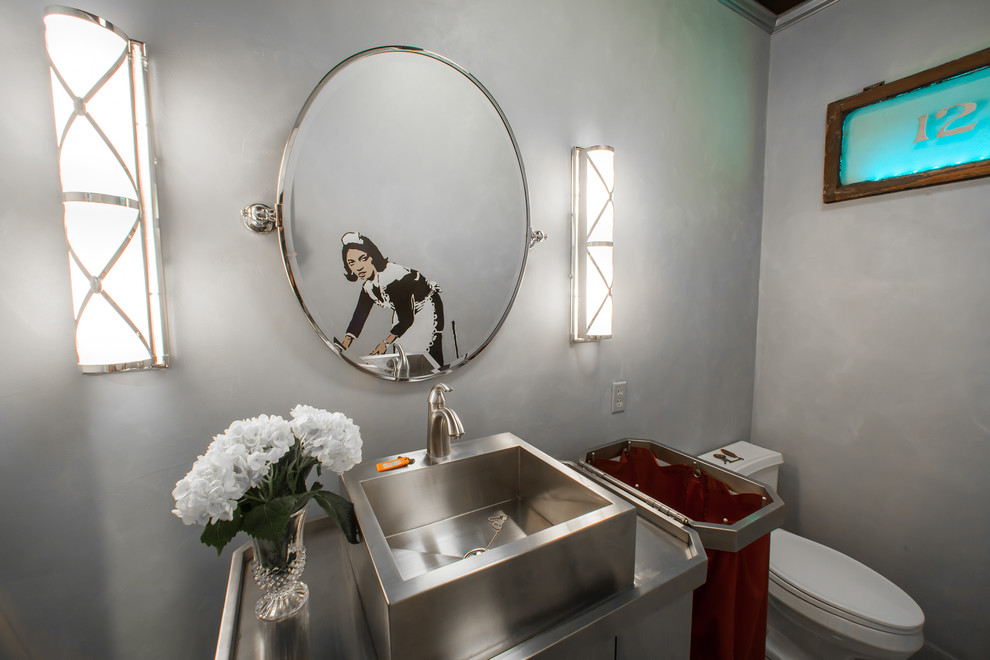 Photo of a mid-sized eclectic powder room in Houston with a vessel sink, furniture-like cabinets, a one-piece toilet, gray tile, grey walls and stainless steel benchtops.