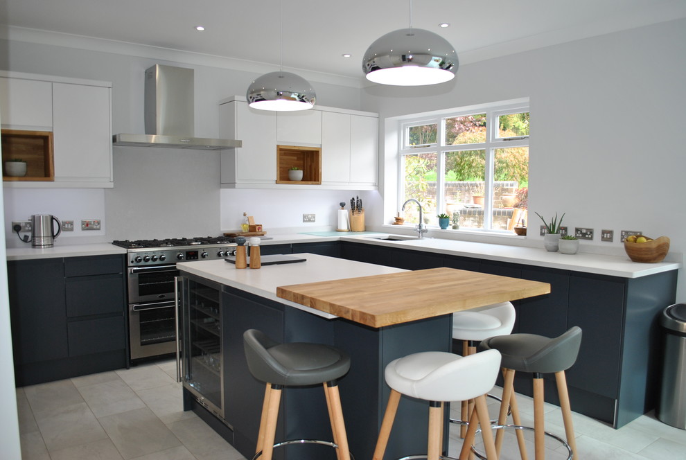 Photo of a mid-sized scandinavian u-shaped separate kitchen in Hertfordshire with a drop-in sink, flat-panel cabinets, stainless steel appliances, with island, grey floor and white benchtop.