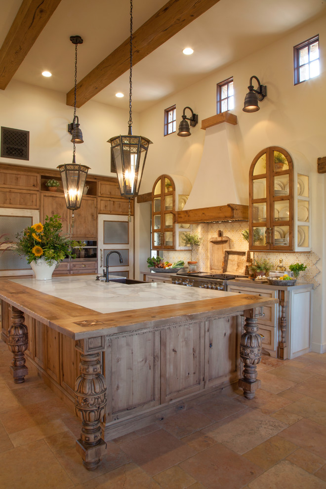 Inspiration for a large mediterranean l-shaped eat-in kitchen in San Diego with a farmhouse sink, recessed-panel cabinets, medium wood cabinets, wood benchtops, beige splashback, mosaic tile splashback, stainless steel appliances, ceramic floors, with island, beige floor, beige benchtop and exposed beam.