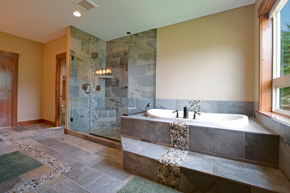 Photo of a large country kids bathroom in Seattle with an undermount sink, shaker cabinets, medium wood cabinets, granite benchtops, a drop-in tub, a double shower, a one-piece toilet, multi-coloured tile, pebble tile and beige walls.