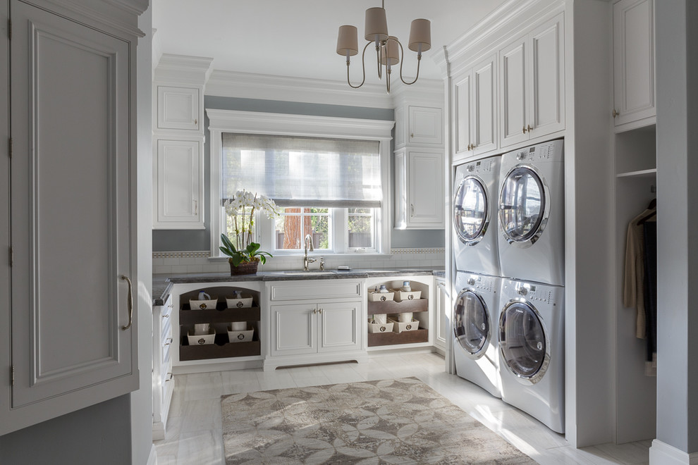 Traditional u-shaped laundry room in San Francisco with an undermount sink, recessed-panel cabinets, white cabinets, grey walls, a stacked washer and dryer and grey benchtop.