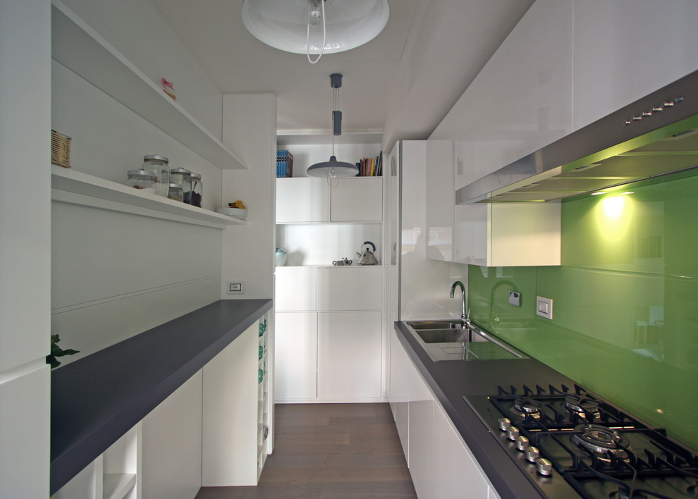 Photo of a small contemporary galley eat-in kitchen in Rome with a drop-in sink, flat-panel cabinets, white cabinets, quartz benchtops, green splashback, glass sheet splashback, stainless steel appliances, medium hardwood floors and with island.