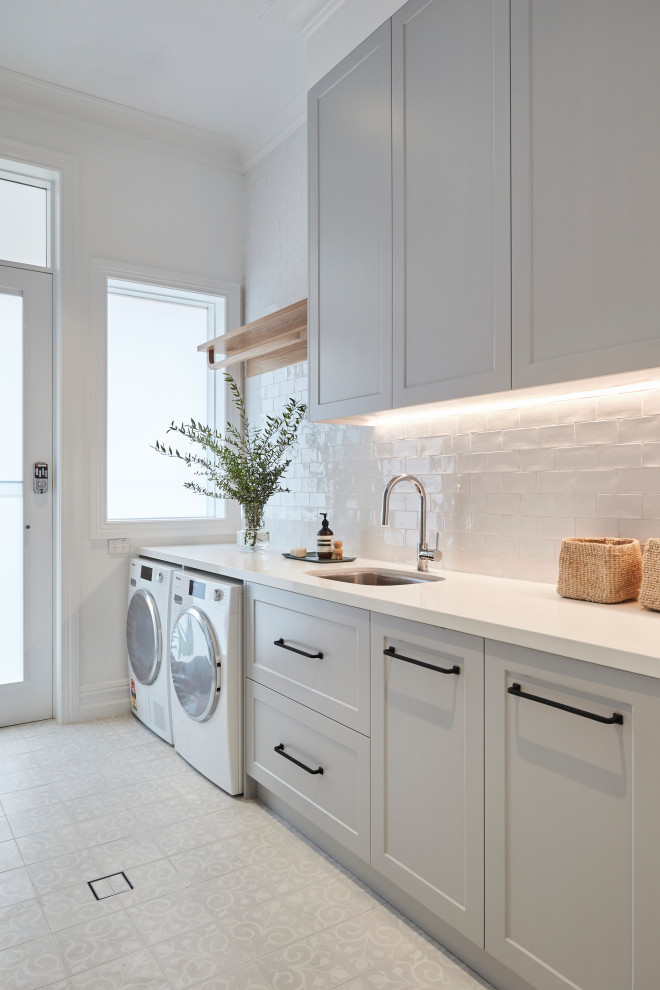 Mid-sized single-wall utility room in Other with shaker cabinets, white cabinets, marble benchtops, glass sheet splashback, grey walls, ceramic floors, a side-by-side washer and dryer, white floor and brown benchtop.