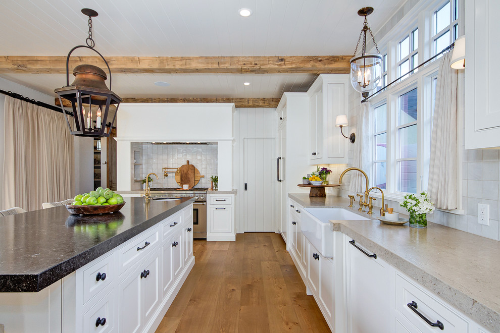 Large country l-shaped eat-in kitchen in Orange County with a farmhouse sink, shaker cabinets, white cabinets, quartzite benchtops, beige splashback, ceramic splashback, stainless steel appliances, light hardwood floors, with island, brown floor and beige benchtop.