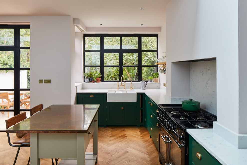 This is an example of a medium sized traditional l-shaped kitchen in London with a belfast sink, shaker cabinets, green cabinets, marble worktops, white splashback, marble splashback, an island, white worktops, a feature wall and medium hardwood flooring.