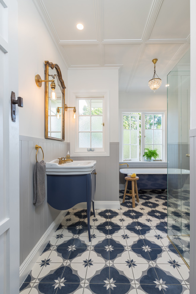 This is an example of a mid-sized traditional bathroom in Auckland with a claw-foot tub, a curbless shower, gray tile, subway tile, grey walls, cement tiles, blue floor, a hinged shower door, white benchtops, blue cabinets, a console sink and flat-panel cabinets.