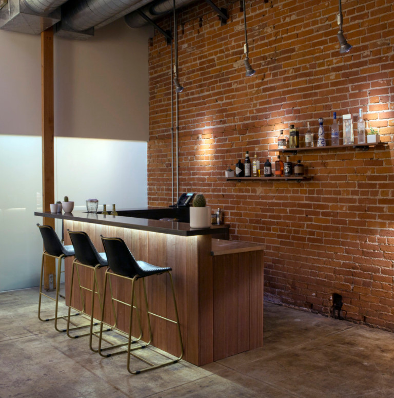 Inspiration for a mid-sized industrial l-shaped seated home bar in Los Angeles with open cabinets, solid surface benchtops, red splashback, brick splashback, concrete floors and grey floor.