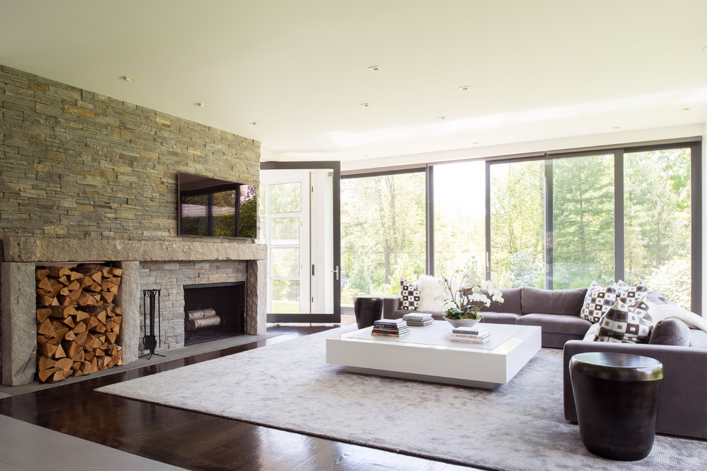 Inspiration for a contemporary open concept family room in New York with dark hardwood floors, a standard fireplace, a stone fireplace surround and a wall-mounted tv.