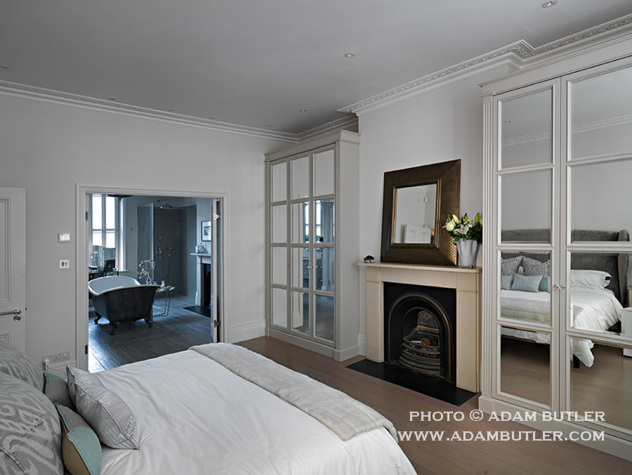 Mid-sized contemporary master bedroom in London with grey walls, medium hardwood floors, a standard fireplace and a wood fireplace surround.