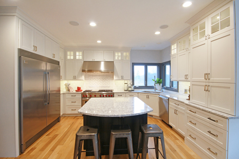 This is an example of a large transitional u-shaped eat-in kitchen in Grand Rapids with an undermount sink, shaker cabinets, white cabinets, quartz benchtops, white splashback, subway tile splashback, stainless steel appliances, medium hardwood floors and with island.
